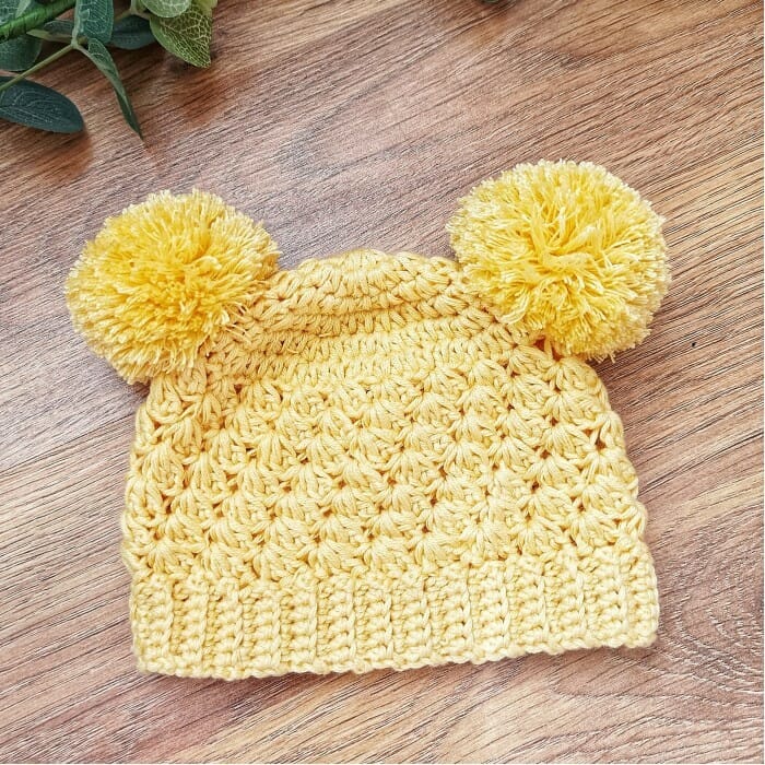 Un bebé con gorro amarillo y un osito con gorro tejido a crochet